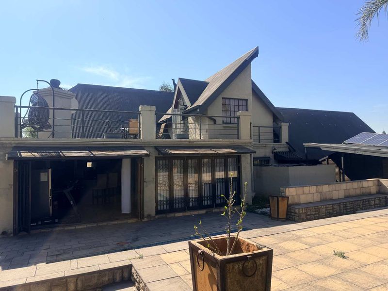 Rear exterior view featuring a paved patio area, upper balcony with metal railings, and folding glass doors leading into the home.
