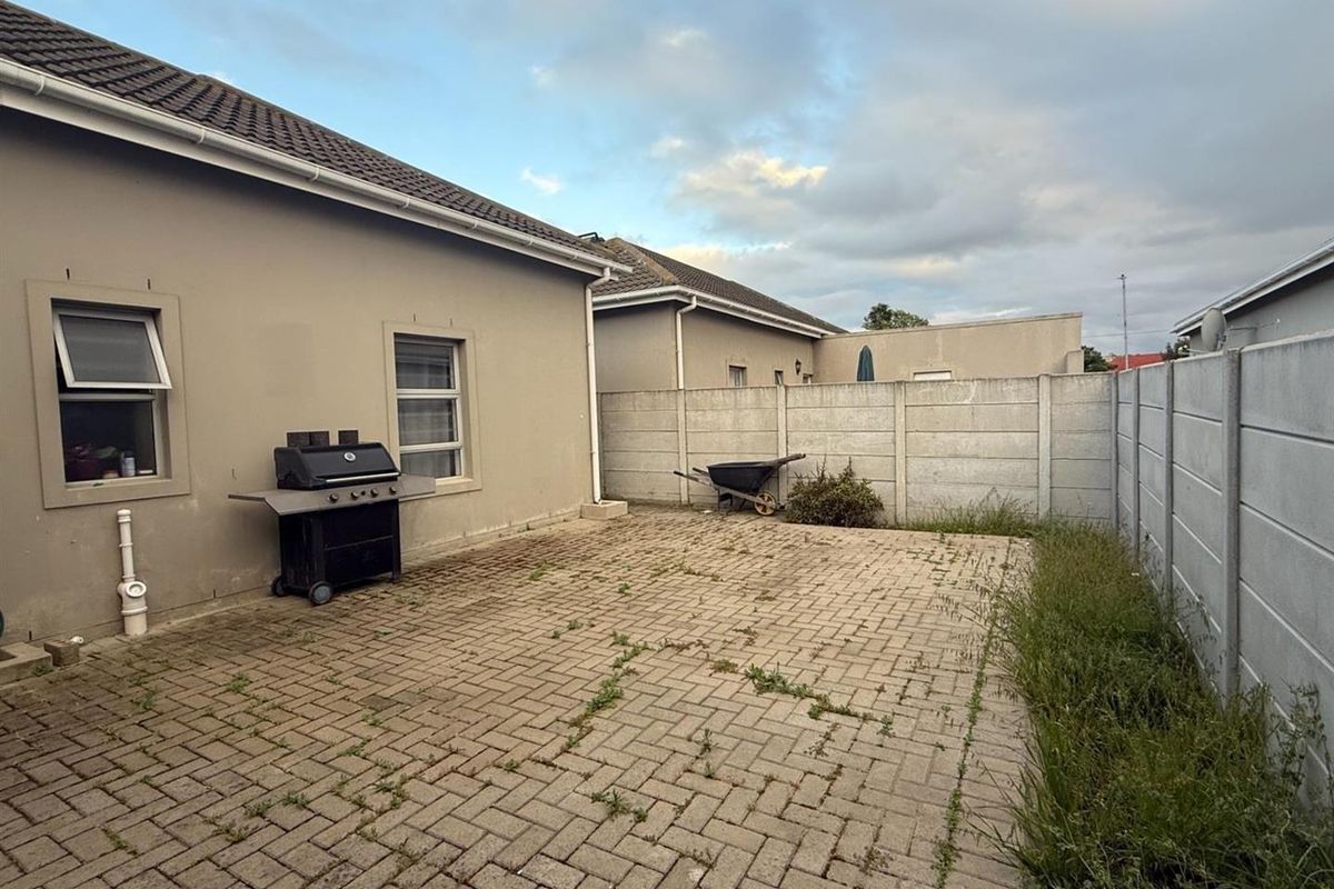 A paved rear courtyard area featuring a concrete boundary wall and exterior access to the main dwelling.