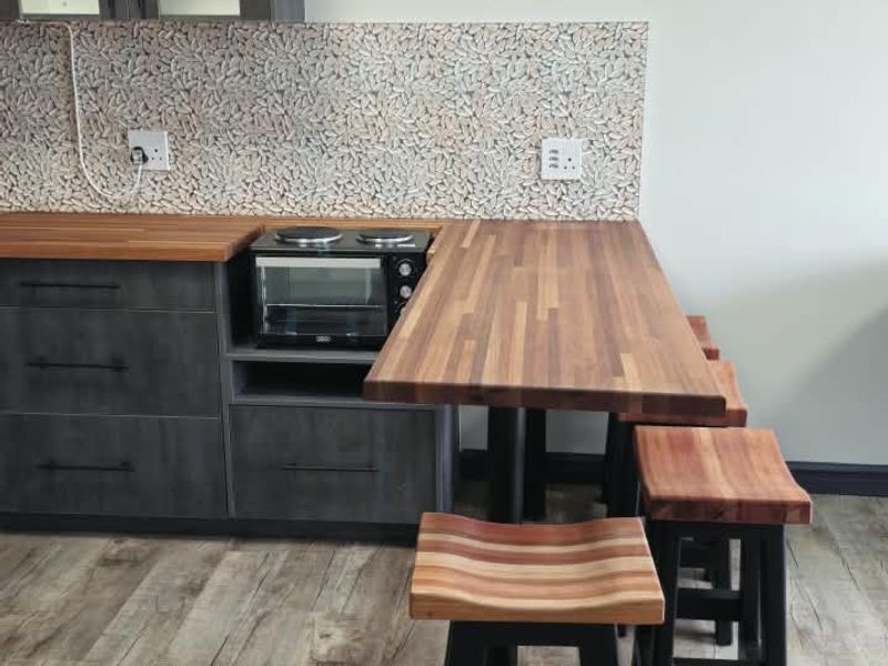 Modern kitchen area featuring dark grey cabinetry, warm wooden countertops, a mosaic tile backsplash, and an integrated breakfast bar with wood-topped stools.