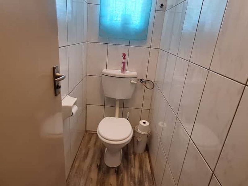 A compact bathroom featuring a standard toilet, full-height ceramic wall tiling, and wood-look laminate flooring.