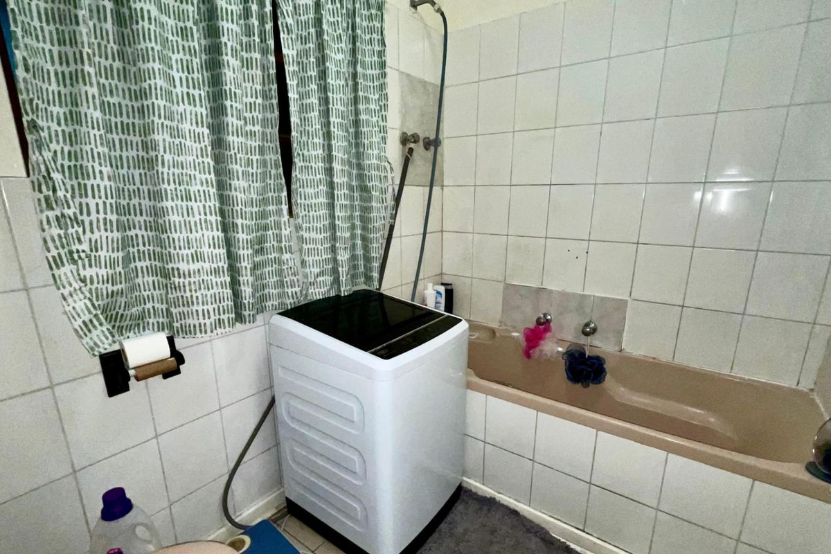 A functional bathroom featuring a bathtub with wall-mounted shower head and tiled splashbacks, currently accommodating a laundry appliance.