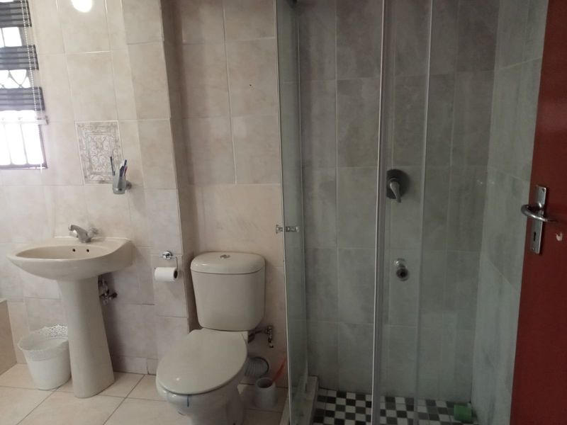 A functional bathroom featuring a pedestal basin, toilet, and a glass-enclosed shower with neutral wall and floor tiling.