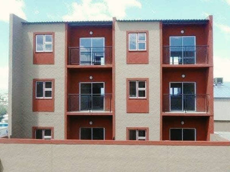 Front elevation of a multi-story apartment building featuring private balconies with metal railings and sliding glass doors on each level.