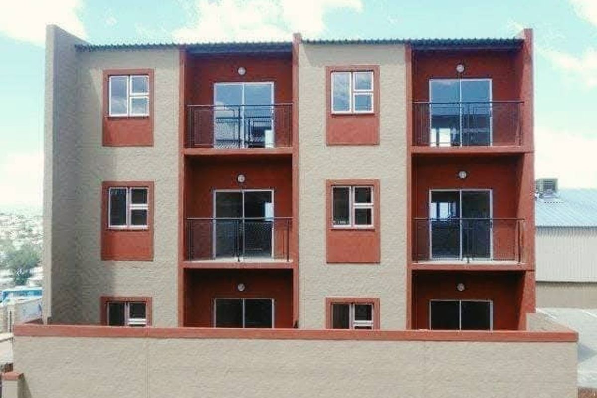 Front elevation of a multi-story apartment building featuring private balconies with metal railings and sliding glass doors on each level.