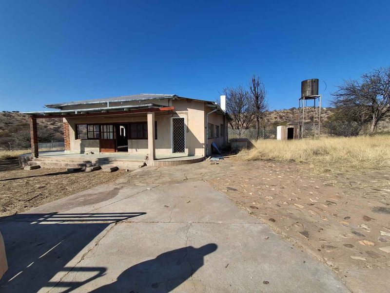 Rear view of a small holding dwelling featuring a covered patio, concrete and stone paving, and an elevated water tank on the property.