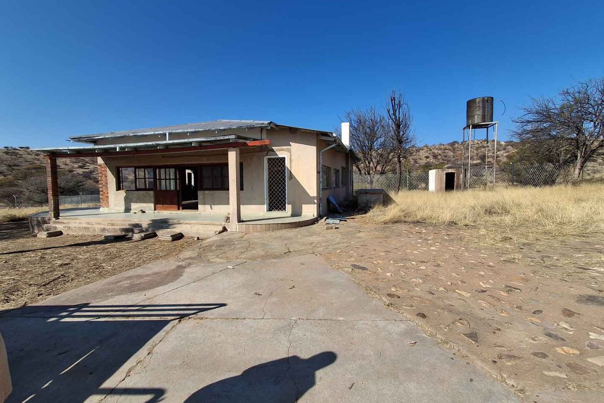 Rear view of a small holding dwelling featuring a covered patio, concrete and stone paving, and an elevated water tank on the property.
