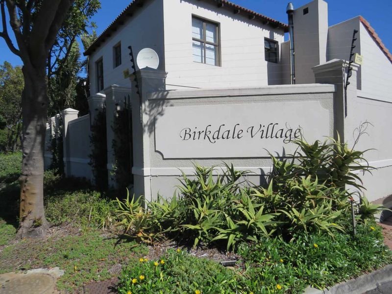 Entrance view of Birkdale Village featuring a plastered boundary wall, electric fencing, and established garden landscaping.