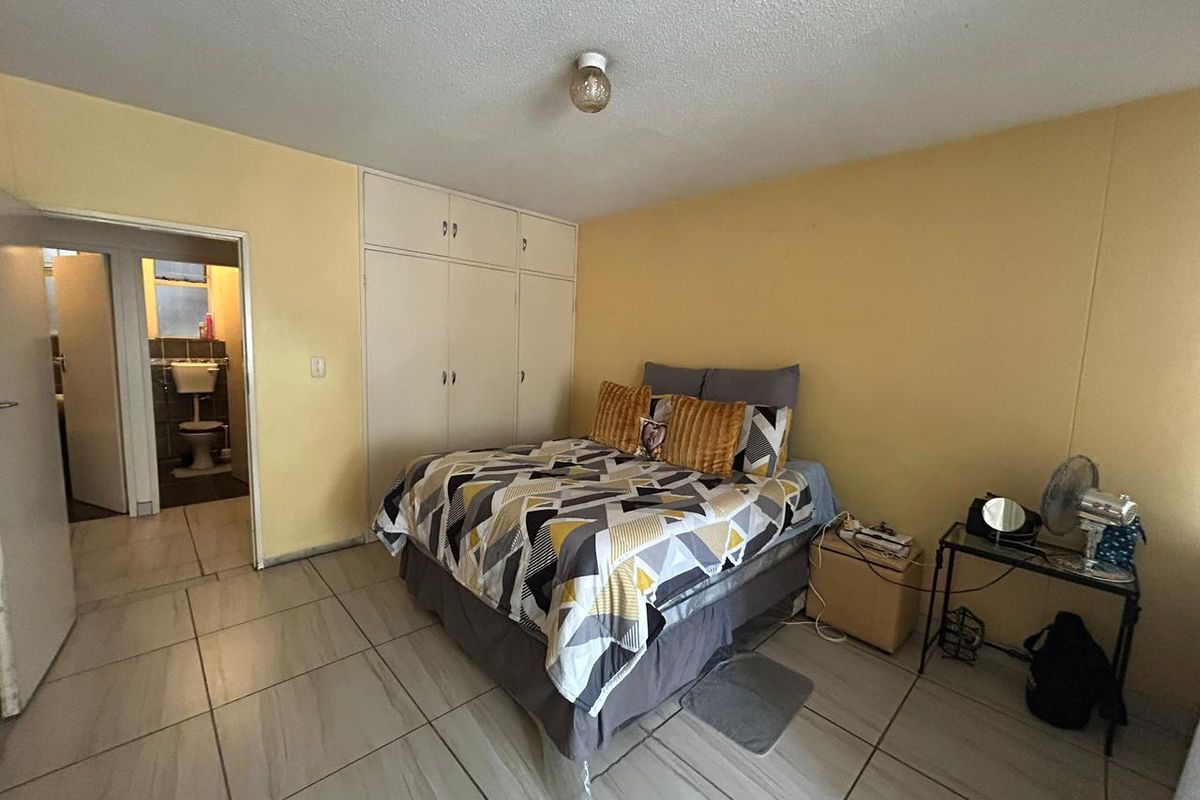 A bedroom featuring built-in cupboards and tiled flooring, with an adjoining bathroom visible through the doorway.