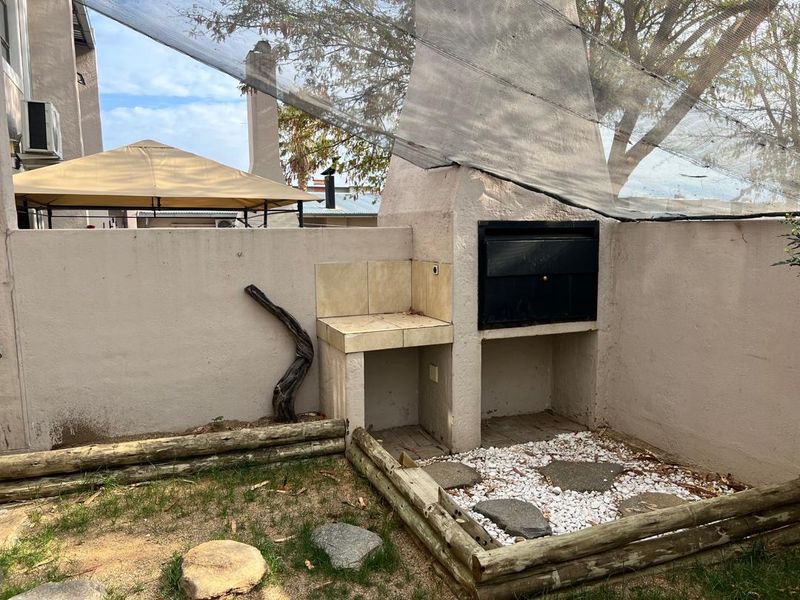 Outdoor entertainment area featuring a built-in braai with tiled prep space and a timber-edged garden bed, requiring some maintenance and landscaping updates.