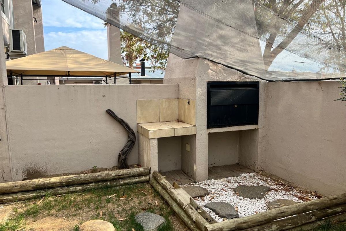 Outdoor entertainment area featuring a built-in braai with tiled prep space and a timber-edged garden bed, requiring some maintenance and landscaping updates.