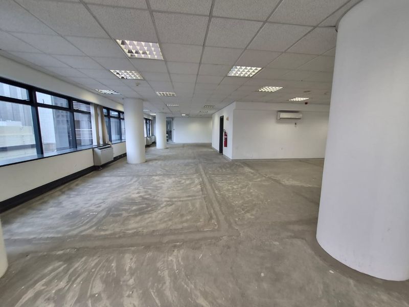 Spacious open-plan office area featuring large windows, suspended ceilings with recessed lighting, and structural columns, currently awaiting floor finishing.