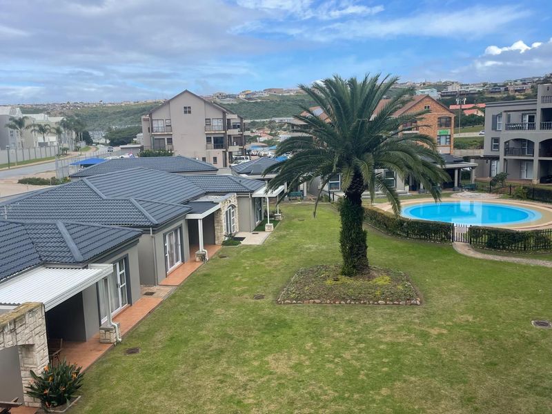 Elevated view of the apartment complex grounds, featuring a communal swimming pool, landscaped garden, and paved patio areas.