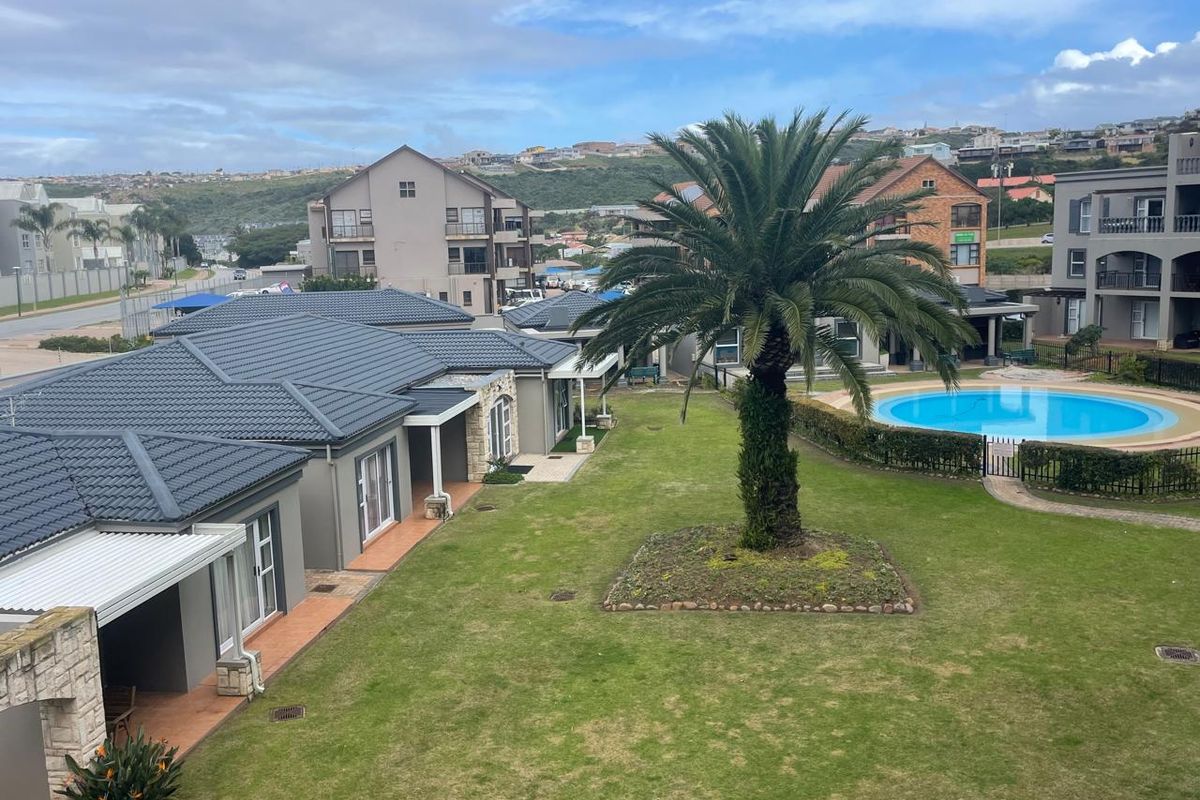 Elevated view of the apartment complex grounds, featuring a communal swimming pool, landscaped garden, and paved patio areas.