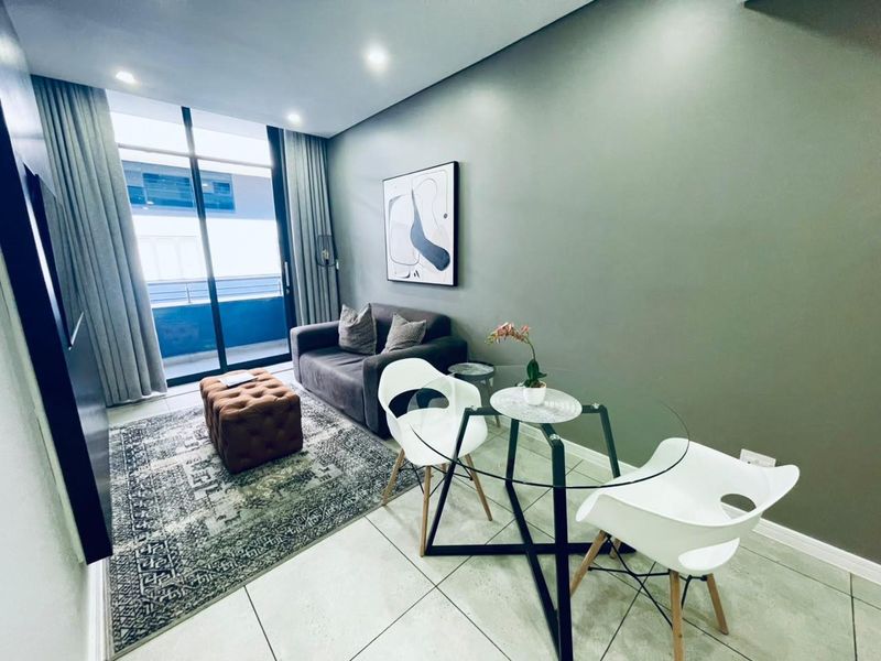 A modern living area featuring tiled flooring, recessed downlighting, and a large sliding glass door providing access to the balcony.