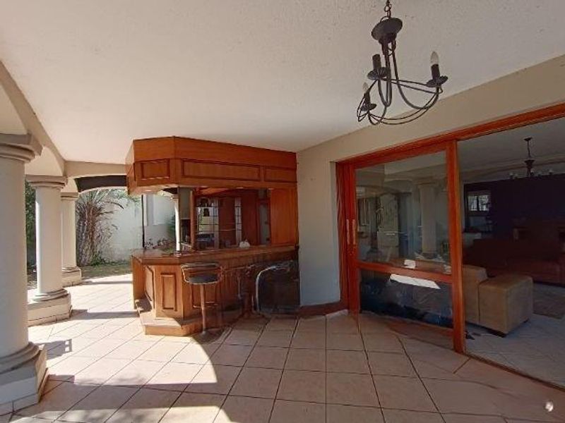 Covered patio area featuring a built-in wooden bar, tiled flooring, and large sliding glass doors providing seamless access to the interior living space.