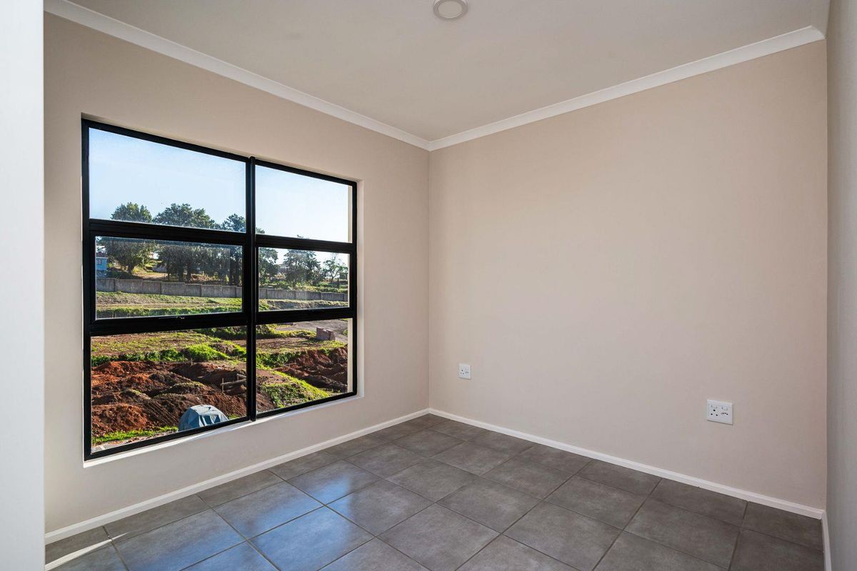 A bright, empty bedroom featuring neutral wall paint, modern grey floor tiles, and a large black-framed window overlooking the surrounding landscape.