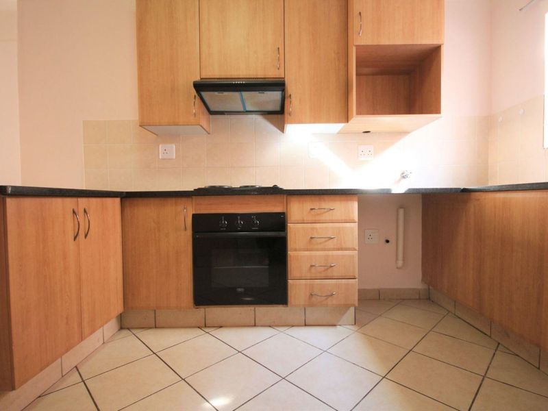 A functional kitchen featuring laminate cabinetry, black granite countertops, built-in oven, hob, and extractor fan with tiled flooring and backsplash.