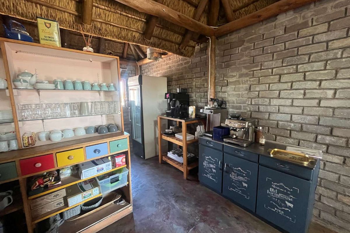 Rustic kitchen area featuring exposed brick walls, a traditional thatched roof, and built-in cabinetry with a concrete floor finish.