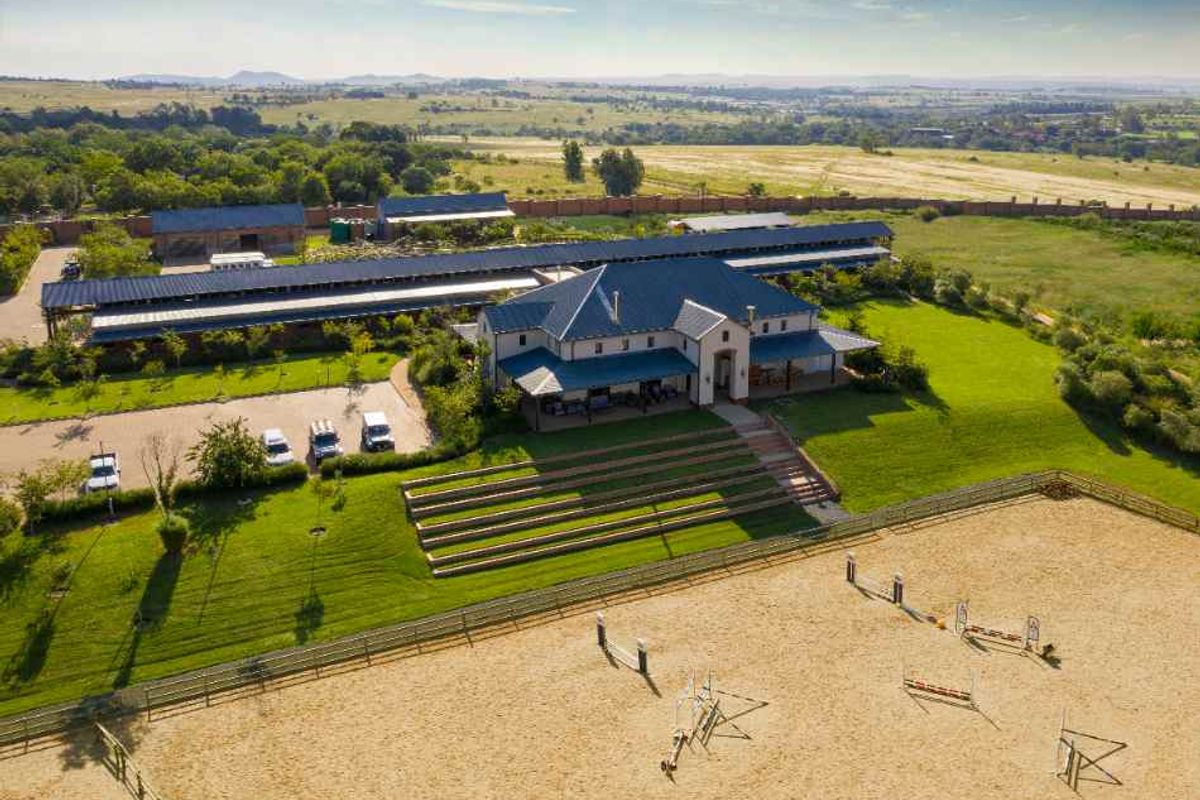 Aerial view of a large equestrian estate featuring a main residence, extensive stable blocks, landscaped grounds, and a professional sand riding arena.