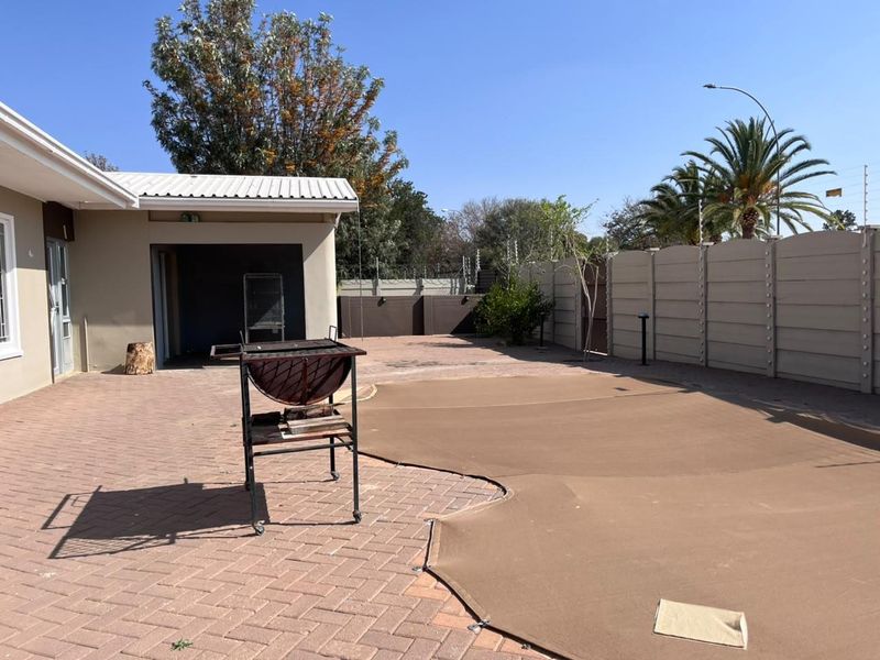 Outdoor entertainment area featuring a paved patio, covered section, and a swimming pool secured with a safety cover, enclosed by perimeter walling.