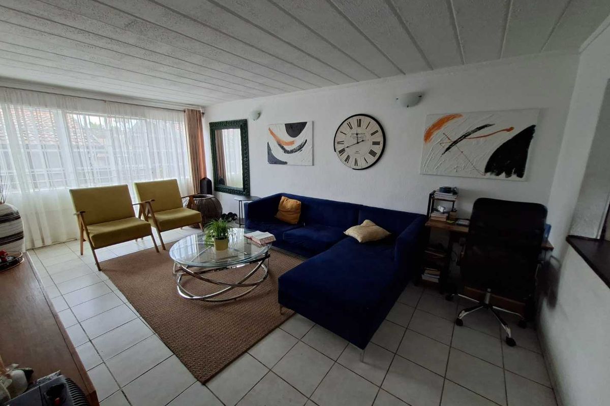 A spacious living room featuring tiled flooring, large windows allowing natural light, and wall-mounted lighting fixtures, providing a comfortable and functional living space.