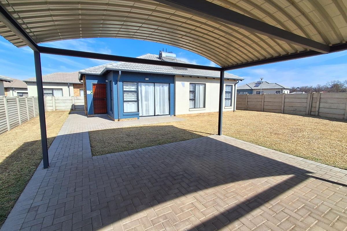 Rear view of the property featuring a paved patio area with a covered carport, enclosed by precast boundary walls and a well-maintained garden.