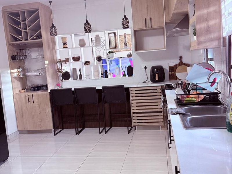 Modern kitchen featuring light wood cabinetry, a built-in wine rack, double basin sink, and a breakfast bar area with pendant lighting.