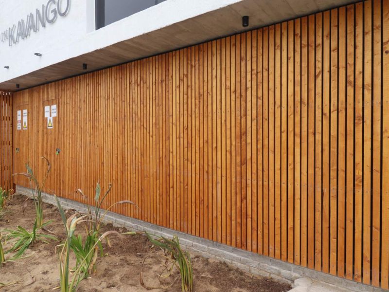Modern building facade featuring decorative timber slat cladding, a concrete overhang with recessed lighting, and clear property signage.