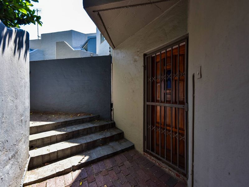 Entrance area featuring a wooden door with a security gate, concrete steps, and brick paving leading to the townhouse entrance.
