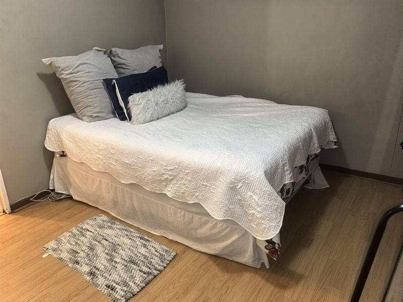 A compact bedroom featuring light-toned laminate flooring and neutral grey wall finishes.