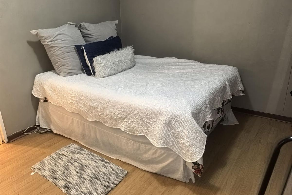 A compact bedroom featuring light-toned laminate flooring and neutral grey wall finishes.