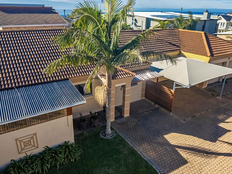 Aerial view of the townhouse front elevation featuring a paved driveway, carport, garage, and well-maintained roof structures.