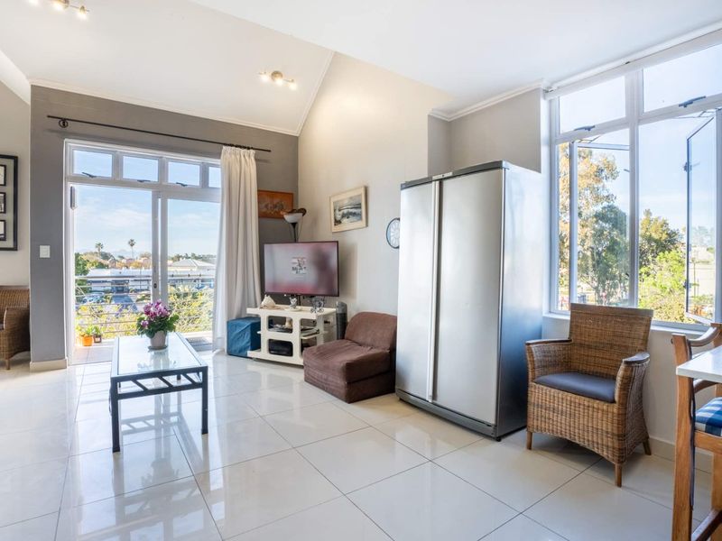 Bright open-plan living area featuring vaulted ceilings, large windows, and direct access to a balcony, creating a spacious and airy atmosphere.