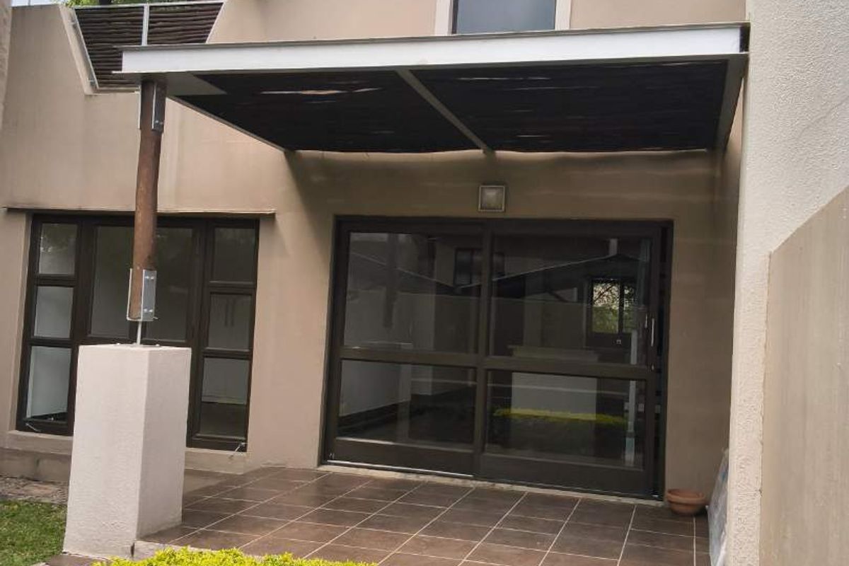 Rear exterior view of the apartment featuring a tiled patio, covered pergola, sliding glass doors, and a traditional thatched roof section.