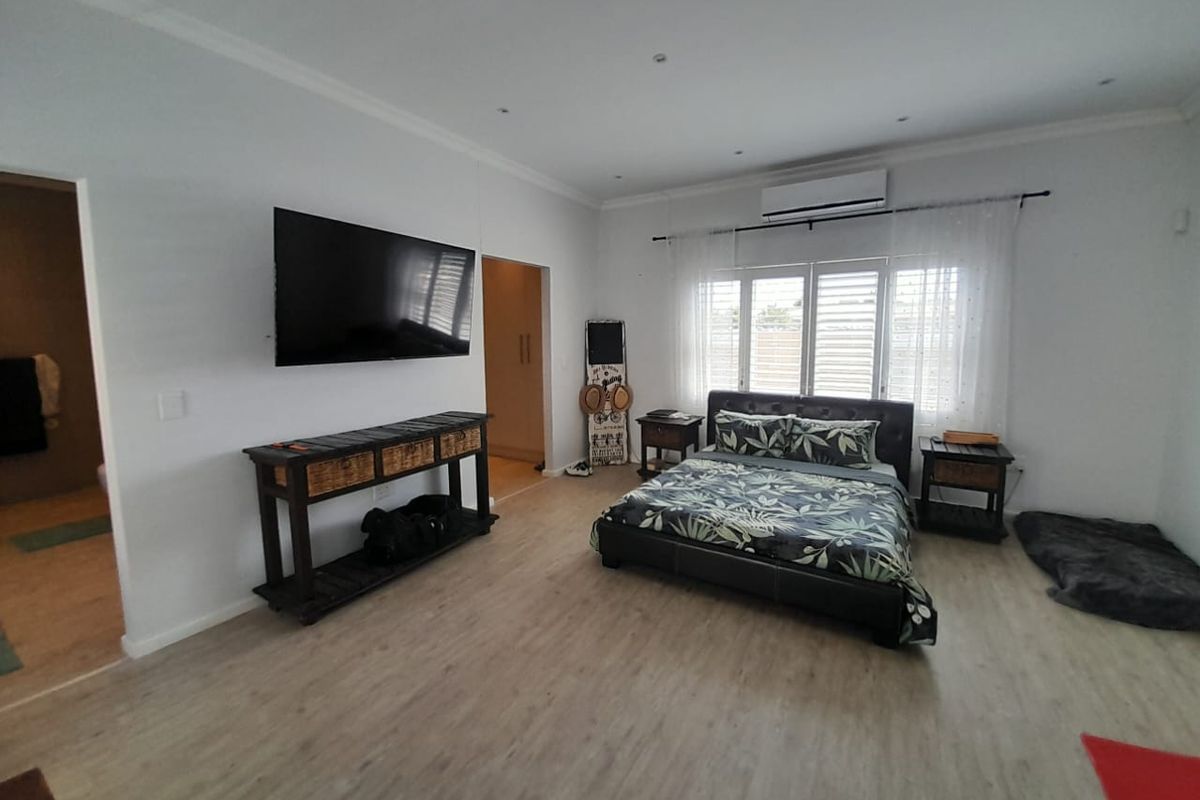 Spacious bedroom featuring light wood-look flooring, recessed ceiling lighting, and a wall-mounted air conditioning unit.
