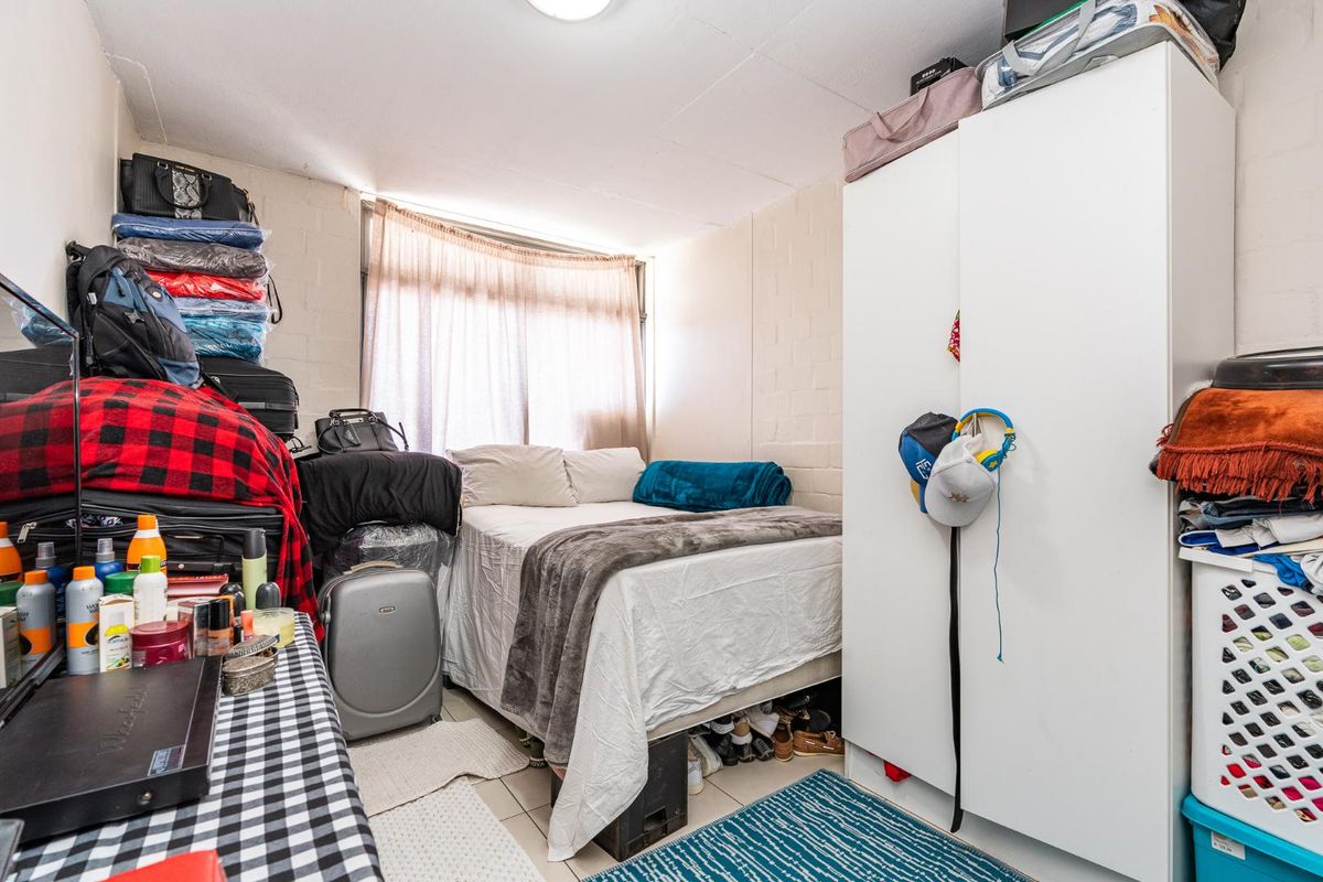 A compact bedroom featuring tiled flooring, a large window with curtains, and a built-in wardrobe.