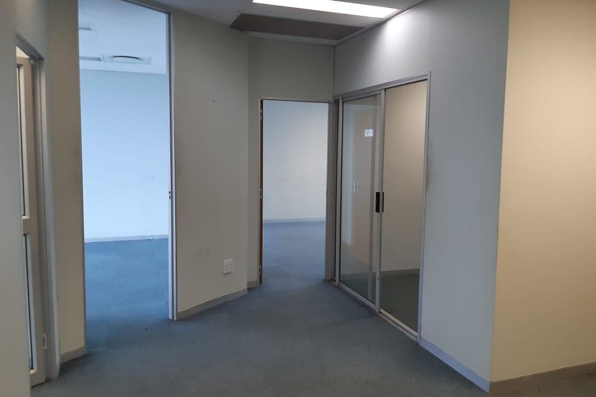 A vacant commercial hallway featuring carpeted flooring, recessed lighting, and multiple internal access points with sliding glass and standard door frames.