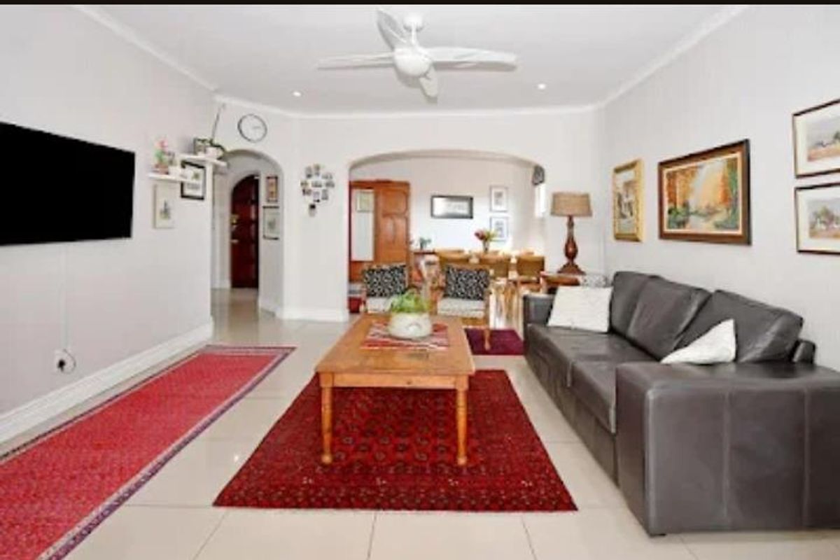 A spacious living room featuring neutral tiled flooring, a ceiling fan, and an arched entryway leading to the dining area.