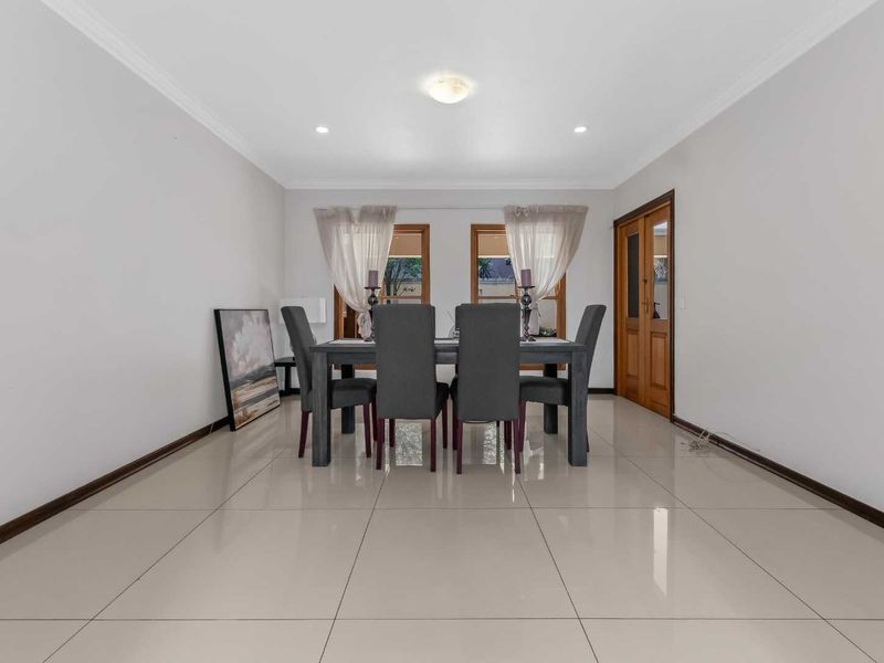 A bright and spacious dining room featuring polished tiled flooring, recessed downlighting, and timber-framed windows and doors.