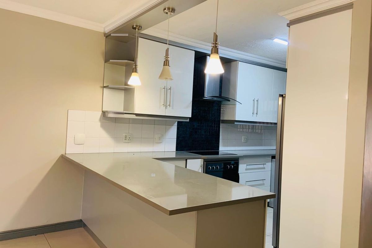 Modern kitchen featuring a breakfast bar, sleek white cabinetry, dark tiled backsplash, and built-in oven with extractor fan.