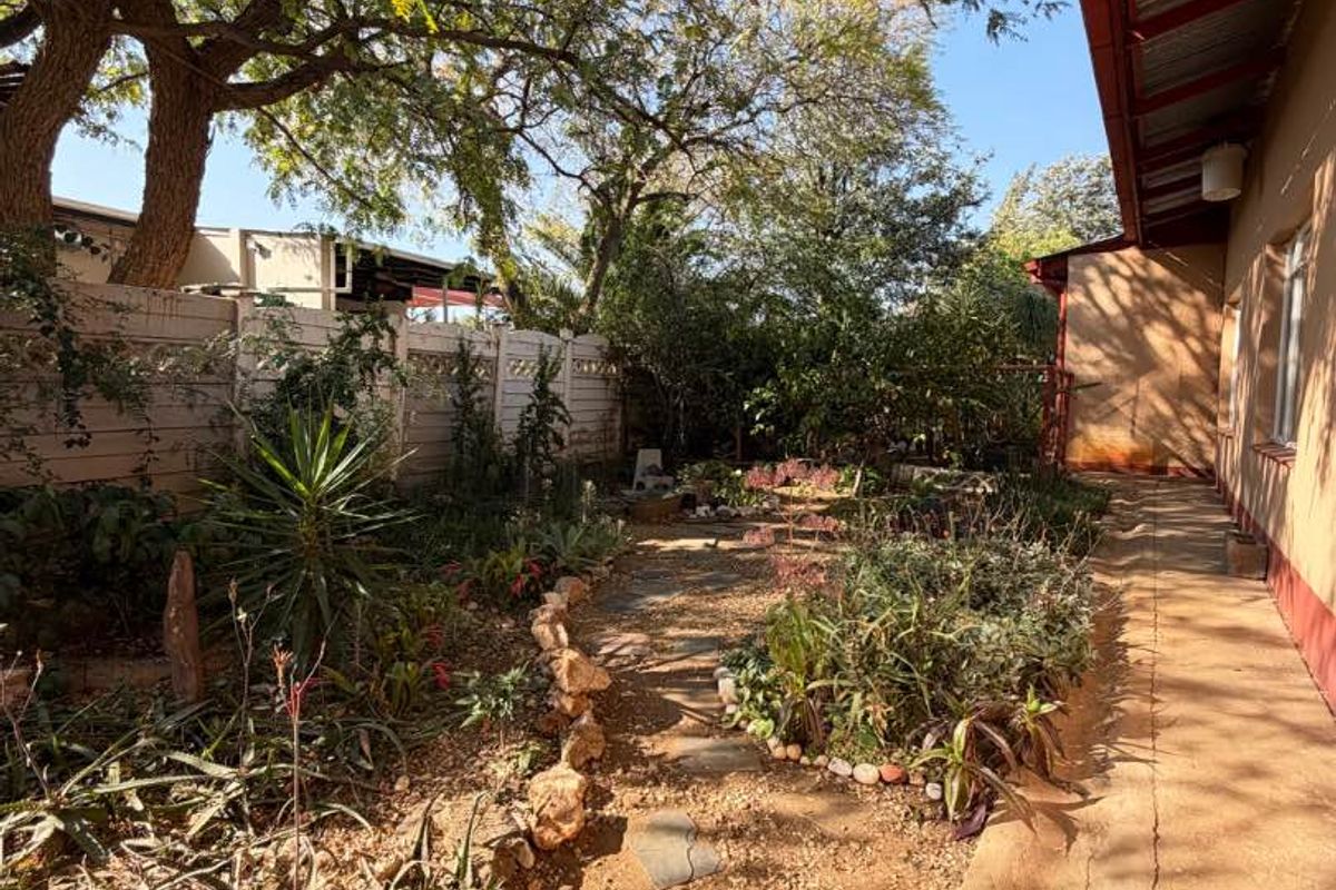 A rear garden area featuring a concrete pathway, established trees, and a precast boundary wall, adjacent to the house's covered exterior walkway.