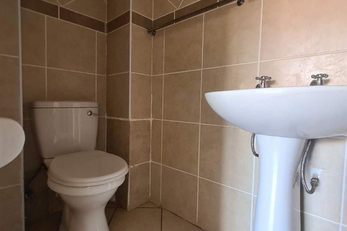 A functional bathroom featuring a pedestal washbasin, ceramic toilet, and full-height wall tiling with a neutral color palette.
