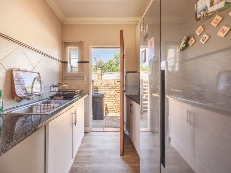 A functional scullery featuring granite countertops, a stainless steel sink, and built-in cabinetry, with direct access to the rear exterior area.
