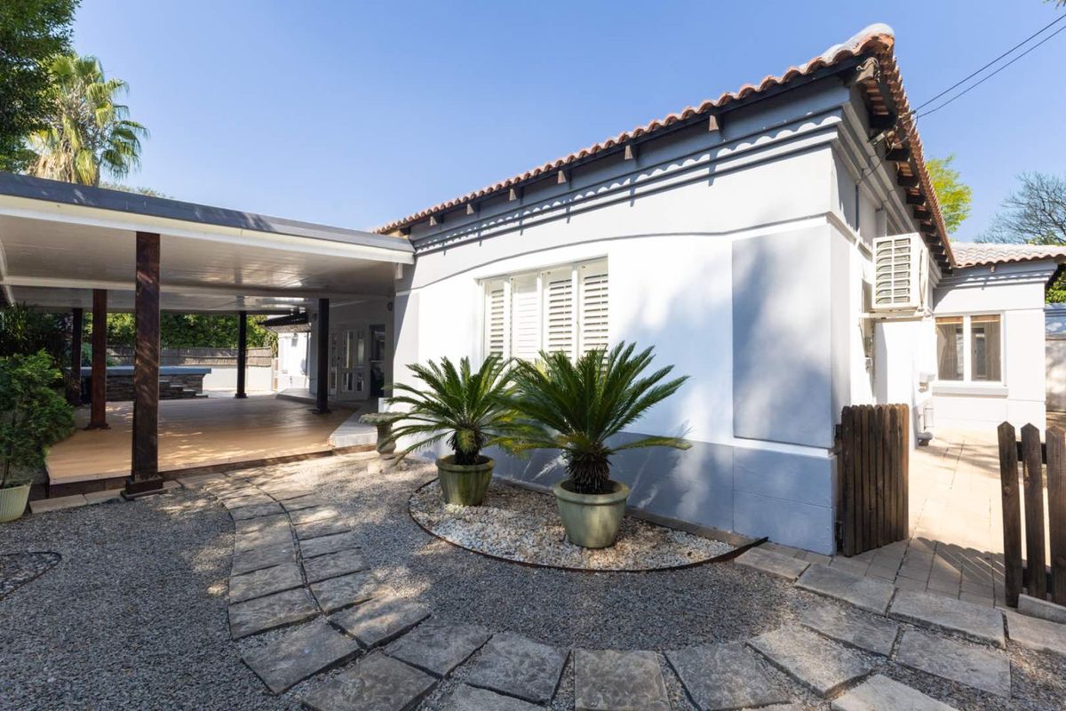 Rear view of the property featuring a covered patio area, stone paved pathway, and well-maintained exterior finishes with terracotta roof tiles.