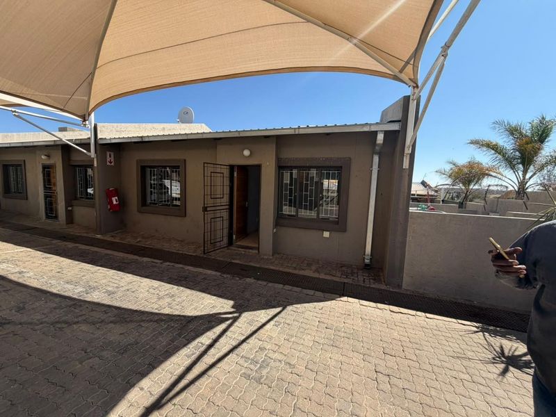 Front exterior view of the townhouse featuring a paved driveway, shade sail covering, and security features including burglar bars and security gates.