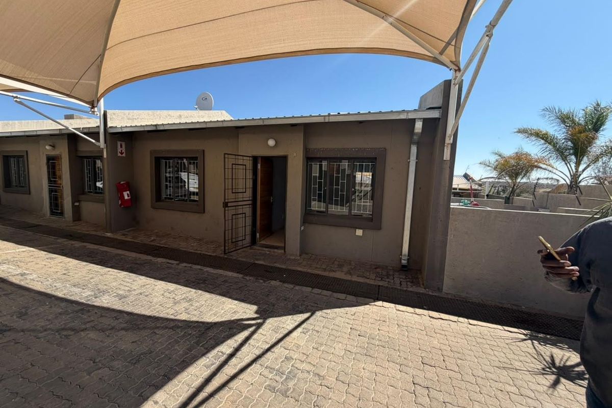 Front exterior view of the townhouse featuring a paved driveway, shade sail covering, and security features including burglar bars and security gates.