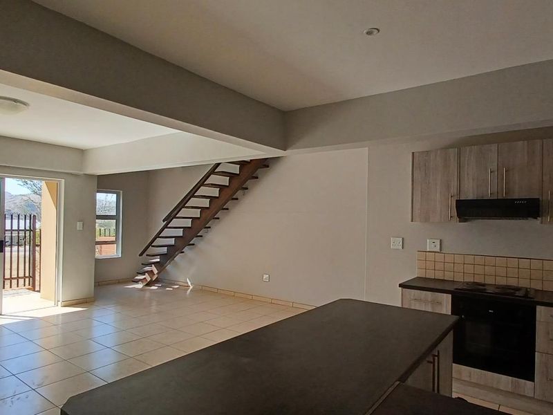 Spacious open-plan living area featuring a modern kitchen with built-in appliances, tiled flooring, and a staircase leading to the upper level.