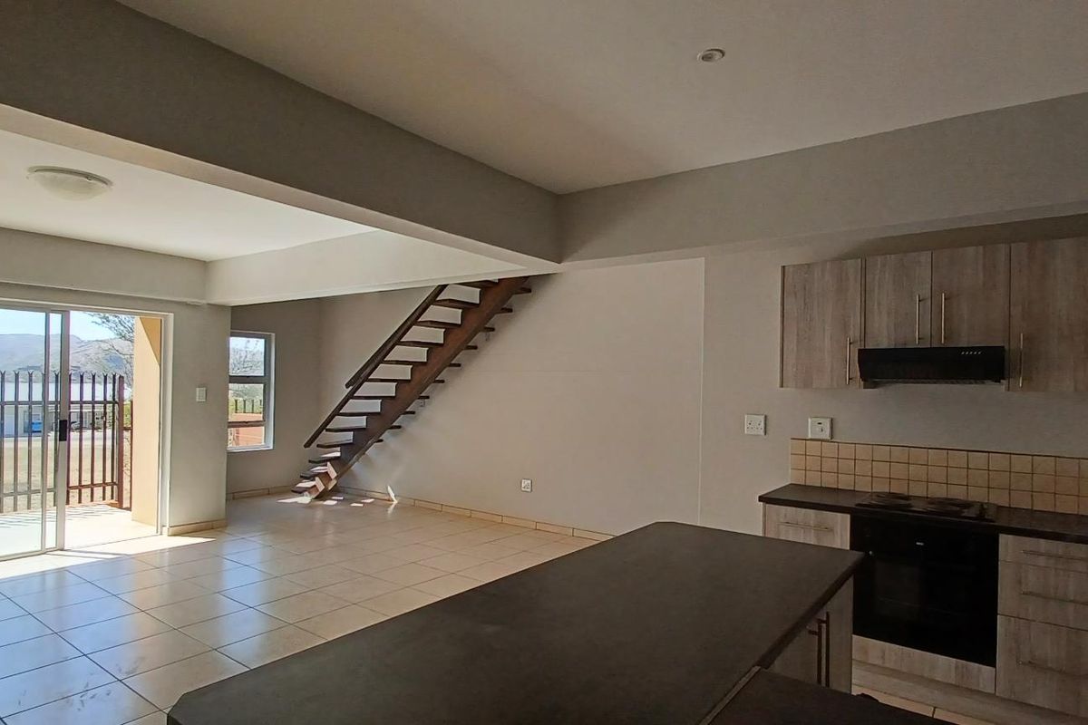 Spacious open-plan living area featuring a modern kitchen with built-in appliances, tiled flooring, and a staircase leading to the upper level.