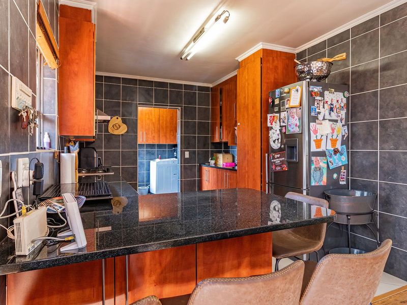 A functional kitchen featuring dark granite countertops, wooden cabinetry, and full-height wall tiling, with an open layout leading to a separate laundry area.