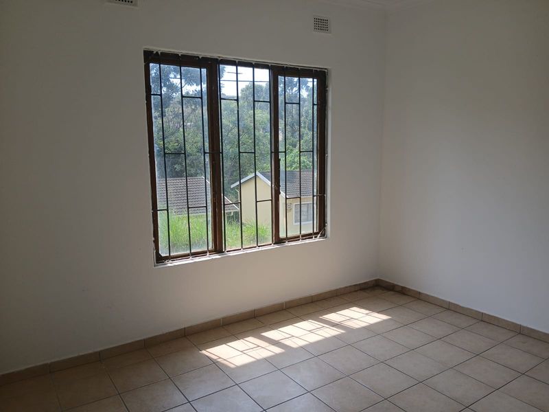 An empty bedroom featuring tiled flooring and a window fitted with security bars, offering a view of the surrounding neighborhood.